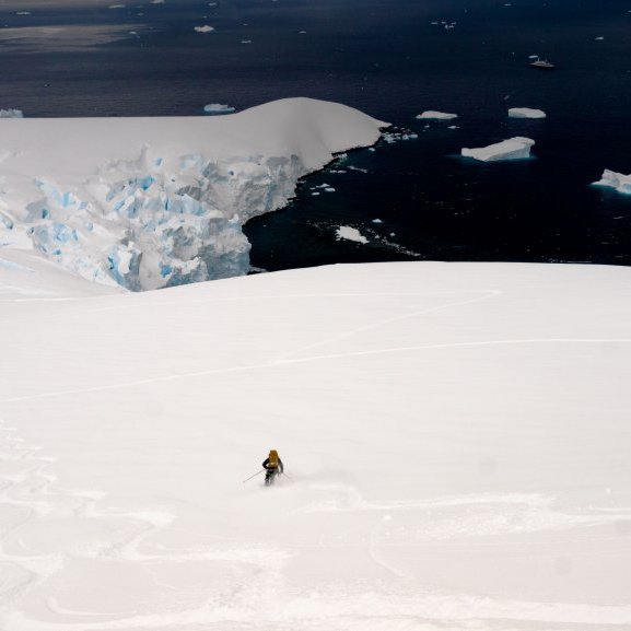 A skier enjoying some fresh snow while skiing down to the shore.